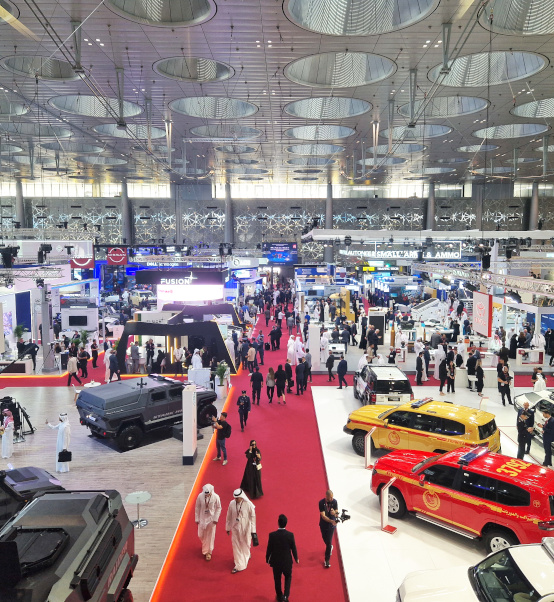 Aerial view of Milipol Qatar 2024 exhibition floor showing stands, vehicles, and visitors