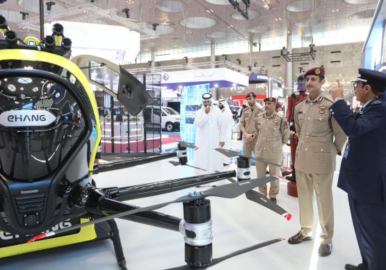 Group of uniformed officers inspecting a drone display at Milipol Qatar 2024 exhibition.