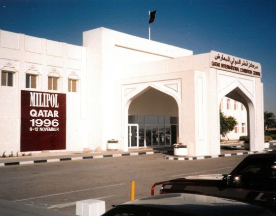 Entrance of the Qatar International Exhibition Center during Milipol Qatar 1996, showing the event banner and cars parked outside.