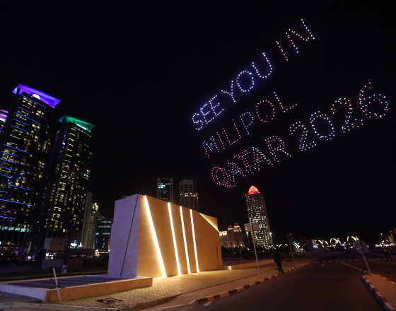 Night view showing a drone light show spelling 'See You in Milipol Qatar 2026' over the city skyline